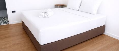Una habitación de hotel moderna con una cama individual, una mesita de noche pequeña y una cama bien hecha con toallas enrolladas.