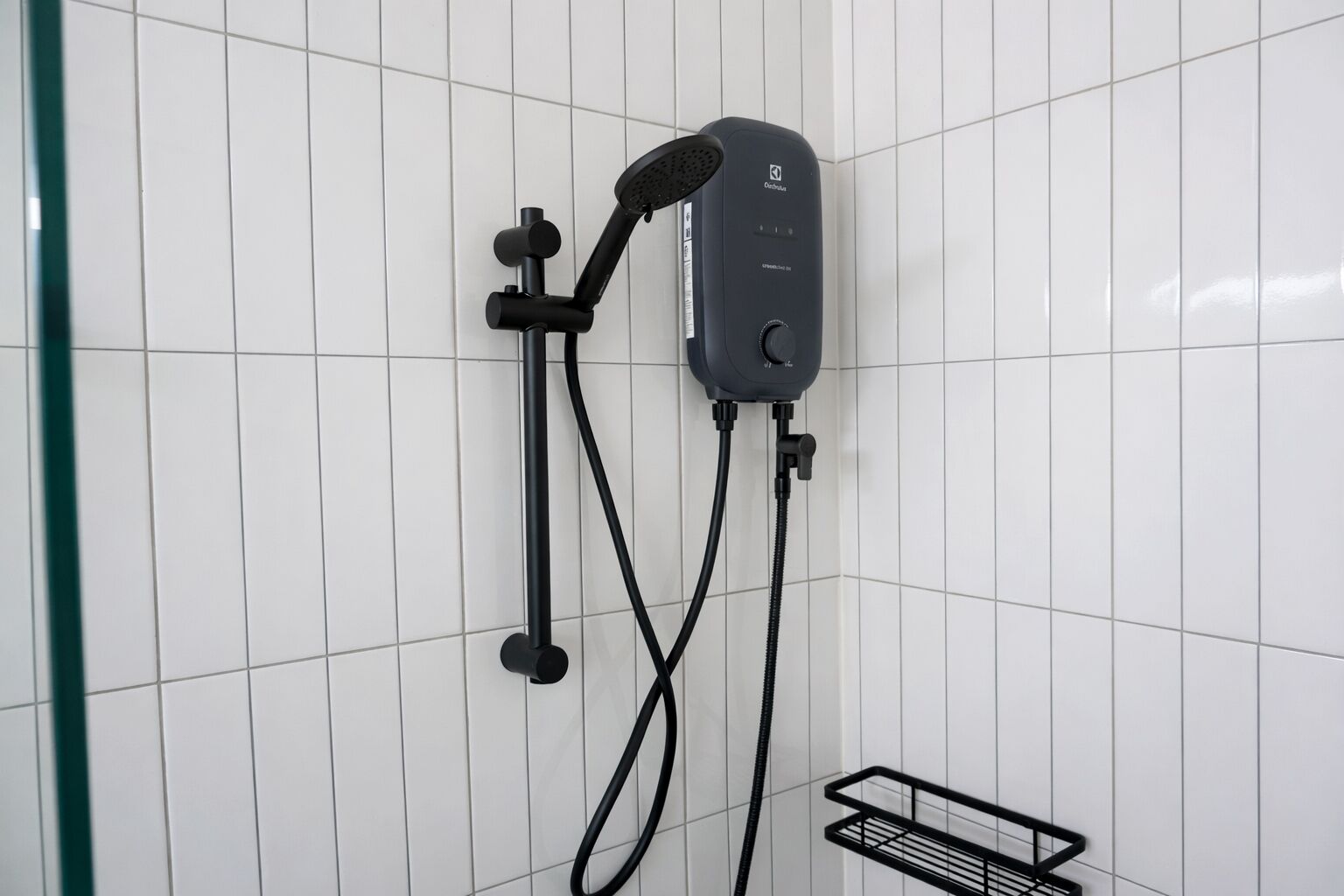 Un cabezal de ducha manual negro fijado a la pared, con una unidad de control y mangueras.