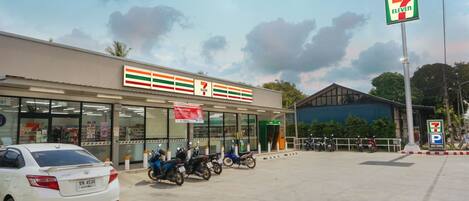 Egy 7-Eleven bolt, amelyen parkolási tábla látható, előtte egy fehér autó és több motorkerékpár parkol.