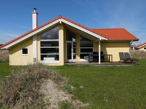 Ein gelbes Haus mit rotem Dach, großen Fenstern und einer Terrasse mit zwei Stühlen.