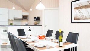Een moderne eetruimte met een lange tafel, zwarte stoelen, witte borden en een fles wijn.