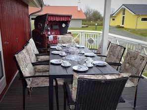 A covered outdoor dining area with a table set for six, surrounded by wicker chairs with floral cushions. - 4 Star Holiday Home in Grossenbrode (Grossenbrode)