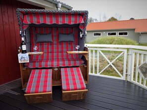 A cozy outdoor seating area with a red and gray checkered sofa, two wooden benches, and a small table with a wine glass. - 4 Star Holiday Home in Grossenbrode (Grossenbrode)
