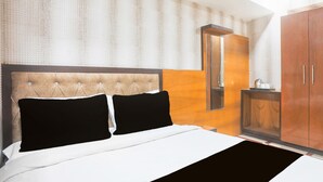 Quarto com cabeceira estofada, cama com roupa de cama preta e branca, guarda-roupa de madeira e espelho na parede.