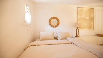 Une chambre à coucher avec un lit, des oreillers, une table de chevet, une lampe et un miroir fixé au mur.