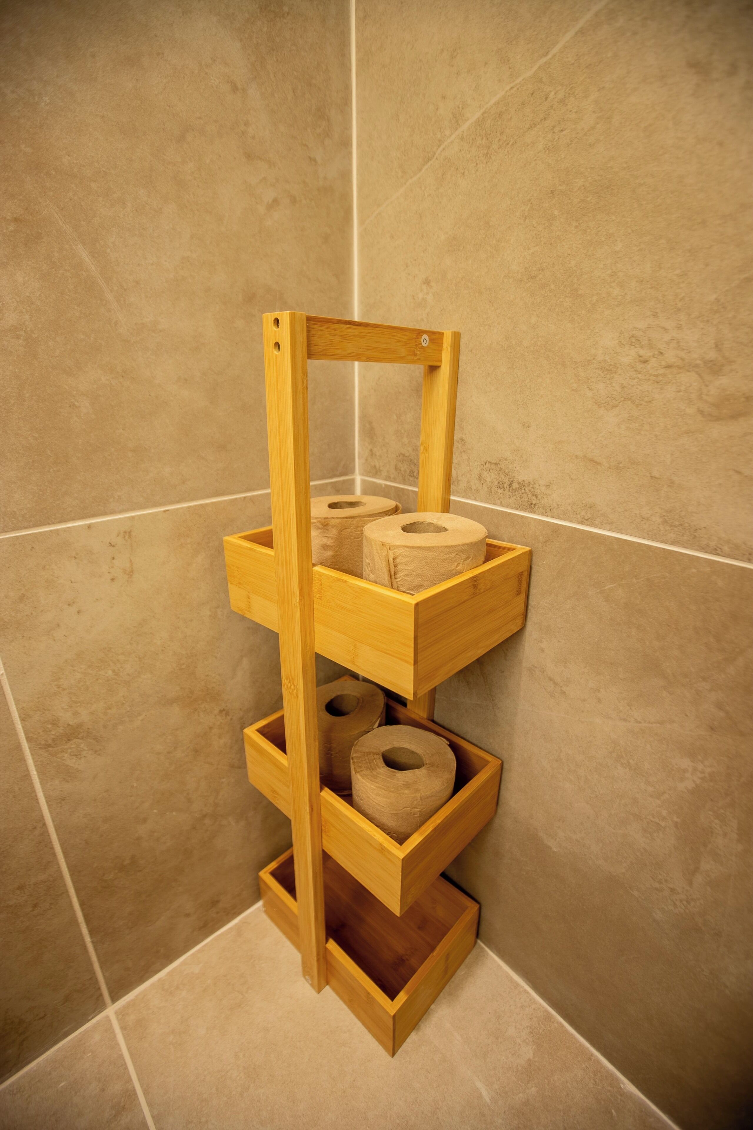 Ein hölzerner Toilettenpapierhalter mit drei Rollen in einem Badezimmer mit beigegefliester Wand.