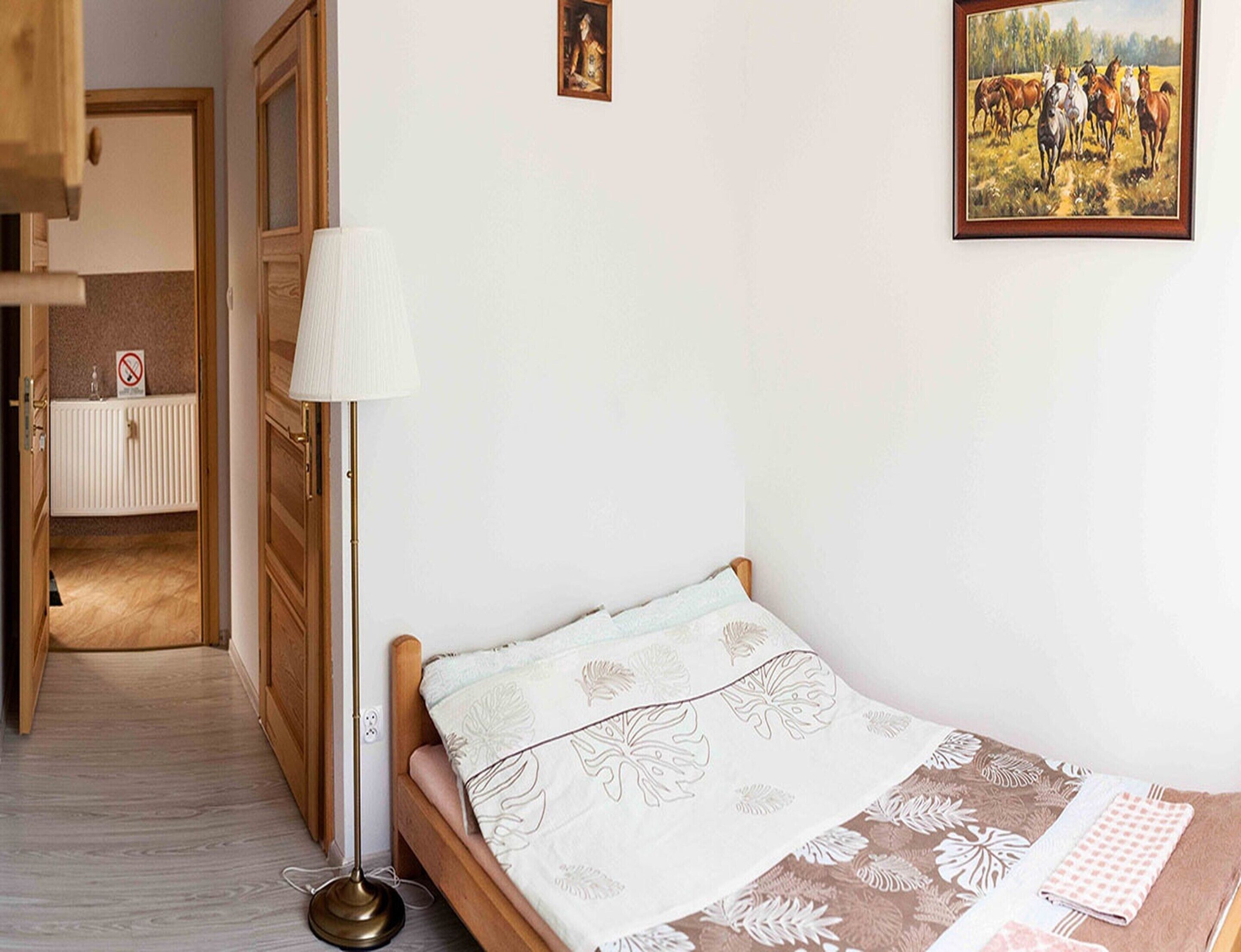 Un dormitorio con una cama individual, una lámpara de noche, un radiador y un cuadro en la pared.