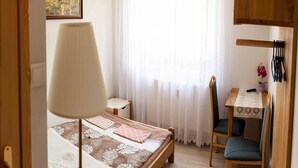 Un dormitorio con cama, una mesita de noche, una silla, un escritorio con silla, una lámpara y un cuadro en la pared.