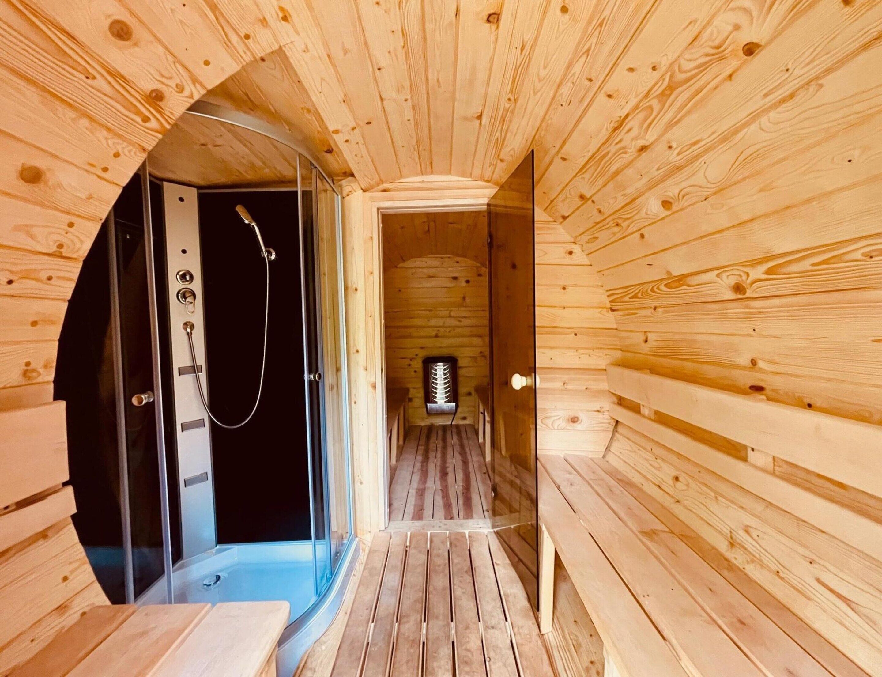 Interior de una cabaña de madera con sauna, un ventanal de vidrio que da a un área de ducha y suelo de madera.
