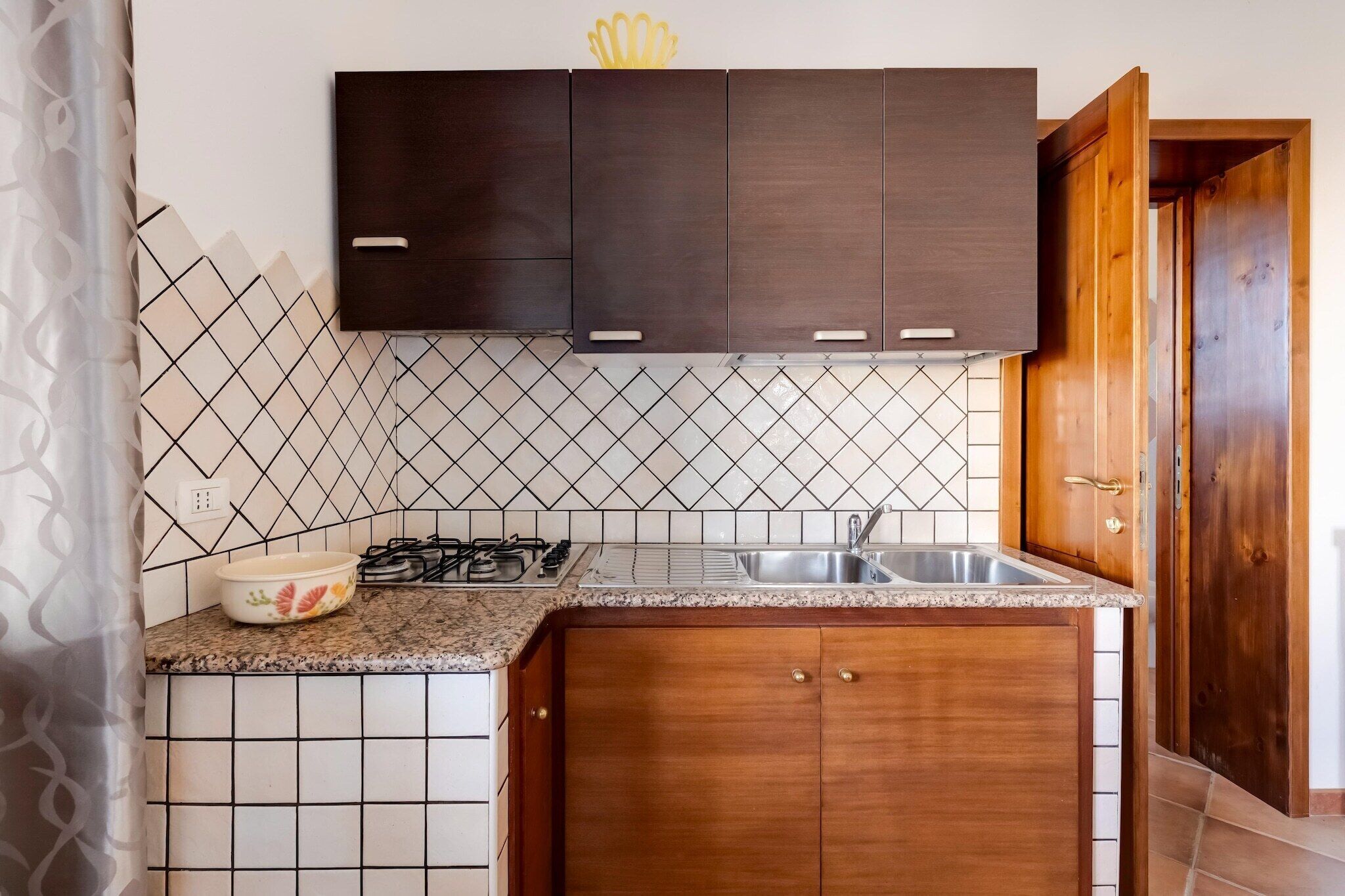 A kitchen with dark wooden cabinets, a tiled backsplash, a granite countertop, a gas stove, and a stainless steel sink.