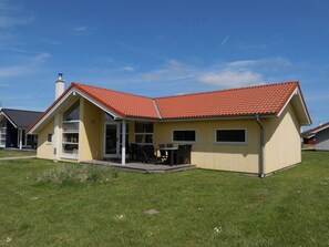 A yellow house with a red roof, a patio with chairs, and a clear blue sky. - 4 Star Holiday Home in Grossenbrode (Grossenbrode)