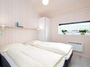 A bedroom with two beds, a window with plants, a radiator, and a white wardrobe. - 4 Star Holiday Home in Grossenbrode (Grossenbrode)