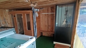 Interior de una cabaña de madera con jacuzzi, paredes de madera y suelo verde.