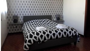 Un dormitorio con una colcha estampada, una mesita de noche con lámpara y un reloj de pared.