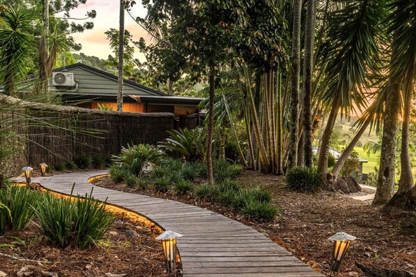 A wooden pathway leading to a house surrounded by tropical vegetation. - Cape Byron Retreat (Skinners Shoot)