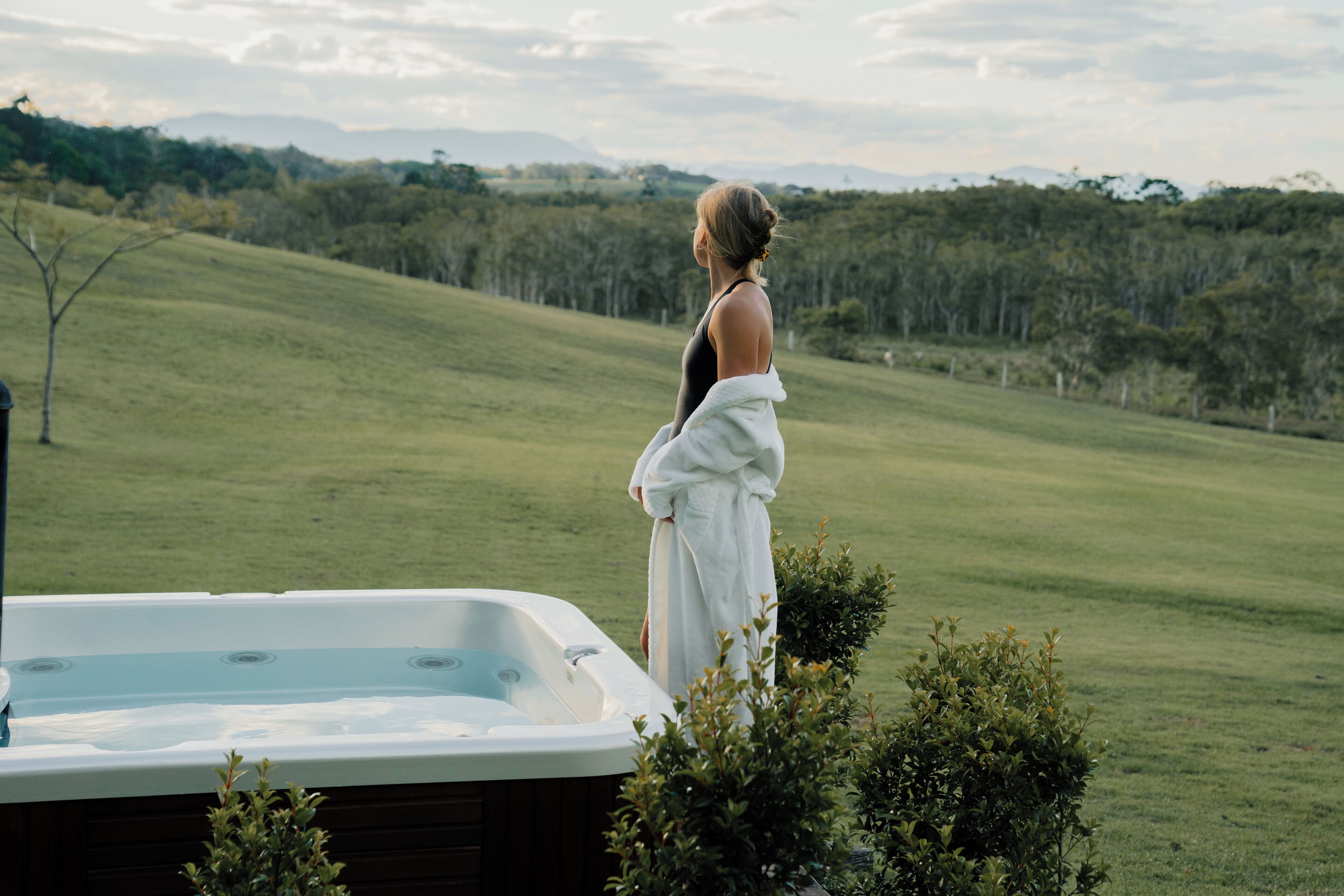 A person standing by a hot tub with a grassy landscape and trees in the background.