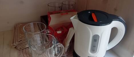 A kitchen area with a white electric kettle, two clear glasses, and a red box of tea bags.