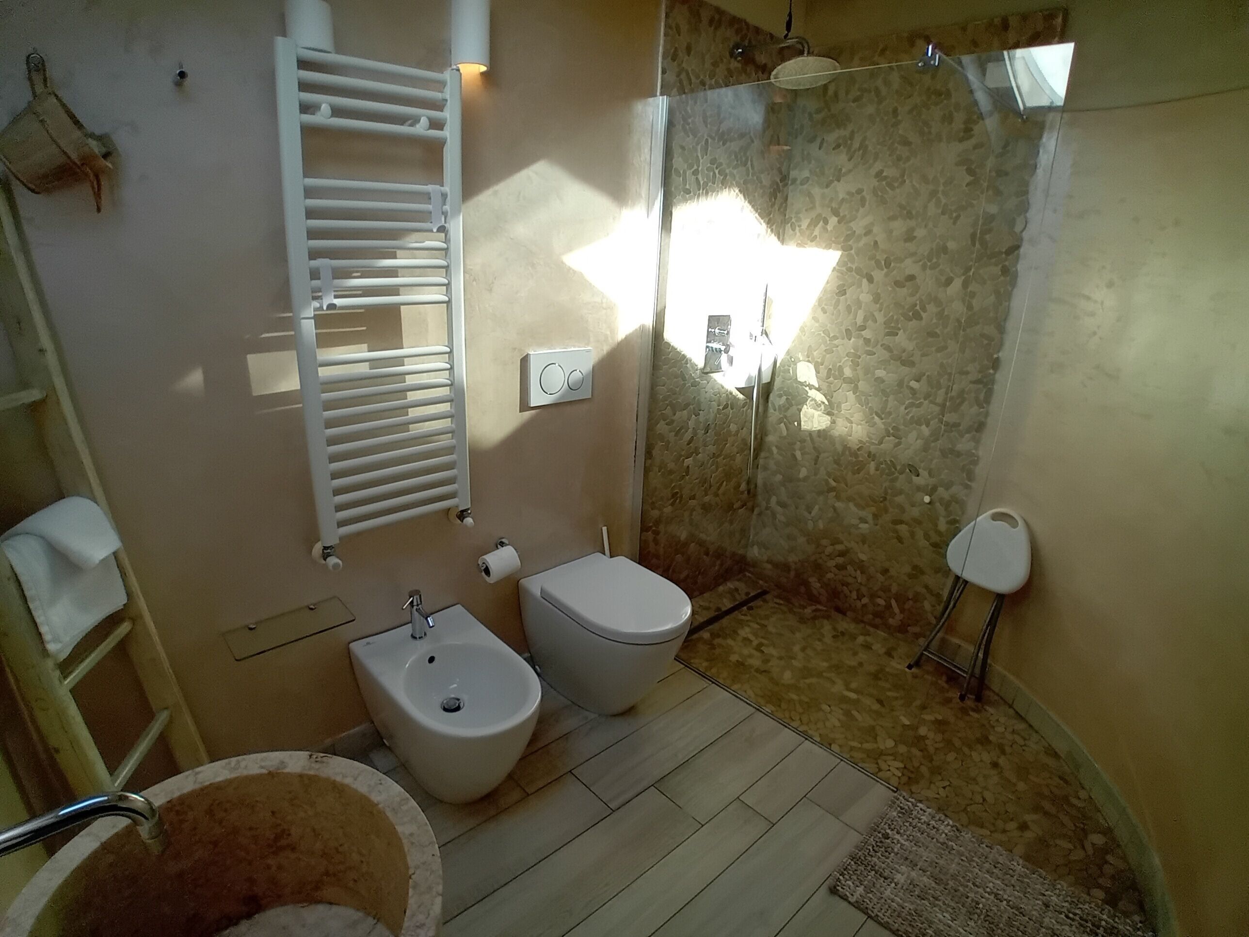 Une salle de bain équipée d’un bidet, de toilettes, d’un porte-serviettes et d’un espace douche avec un mur en pierre.