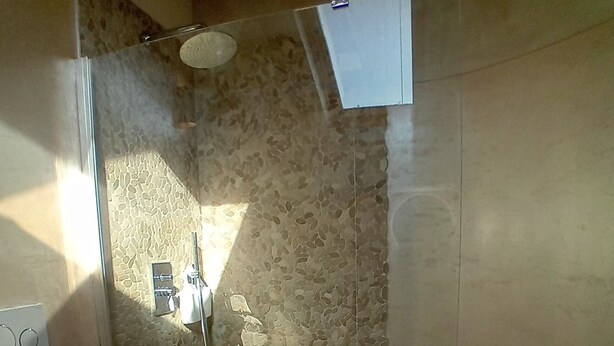A bathroom with a stone wall, a shower, a toilet, and a small stool. - DELUXE DOUBLE ROOM WITH ROUND BED IN THE CENTER OF ALBENGA UP TO 4 PEOPLE (Albenga)