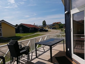 A wooden deck with a table and chairs, overlooking a street with houses and parked cars. - 4 Star Holiday Home in Grossenbrode (Grossenbrode)