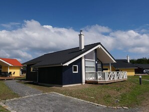 A single-story building with a dark facade, a white porch railing, and a chimney. - 4 Star Holiday Home in Grossenbrode (Grossenbrode)
