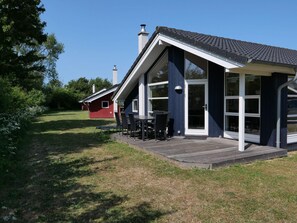Ein modernes Haus mit einer Terrasse, großen Fenstern und einem roten Gebäude im Hintergrund.