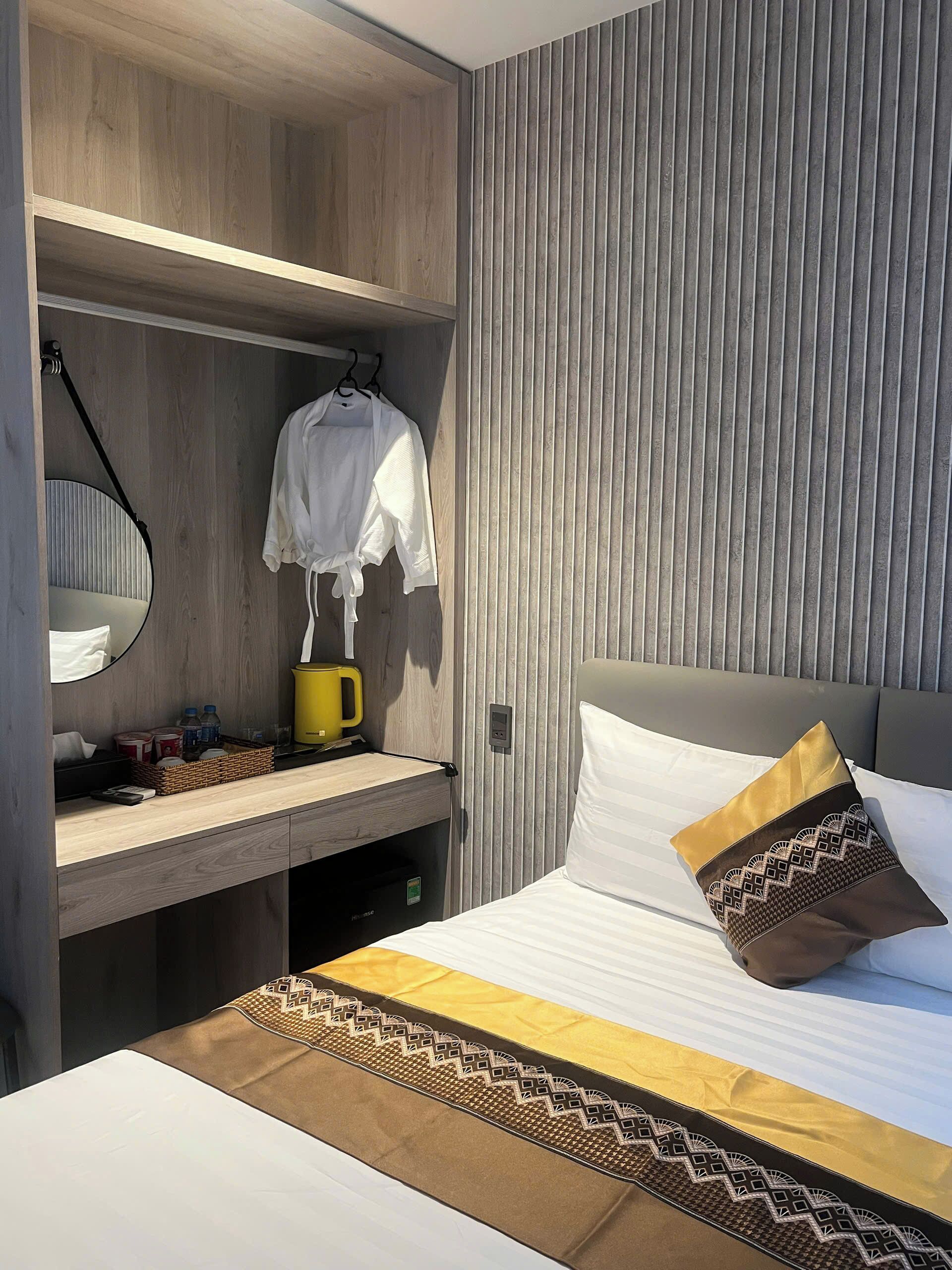 Ein Hotelzimmer mit Bett, Nachttisch, Spiegel, Pendelleuchte und Wandregal.