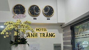 A szálloda recepciójánál órák mutatják New York és Párizs időét, egy nagy, virágzó orchidea áll egy cseredényben, és egy tábla hirdeti: „HOTEL ANH TRANG”.