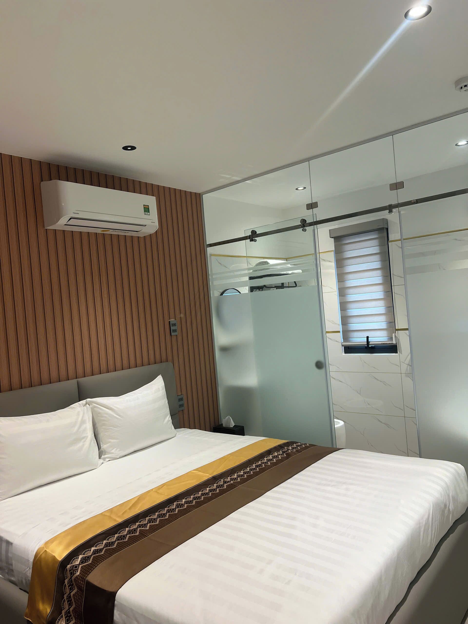 Hotelkamer met een bed, een wandairconditioner, een douchecabine van glas en een raam met zonwering.