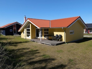 Ein gelbes Gebäude mit rotem Dach, einer überdachten Terrasse mit Stühlen und einem Rasengrundstück.