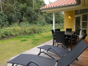 Eine Terrasse mit Tisch und Stühlen, ein Liegestuhl und ein überdachter Bereich mit einem geflasterten Dach.