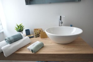 A bathroom with a large white sink, wooden countertop, two rolled towels, a small potted plant, and a mirror above the sink. - G studio near sea central Rapallo/ near Portofino (Rapallo)