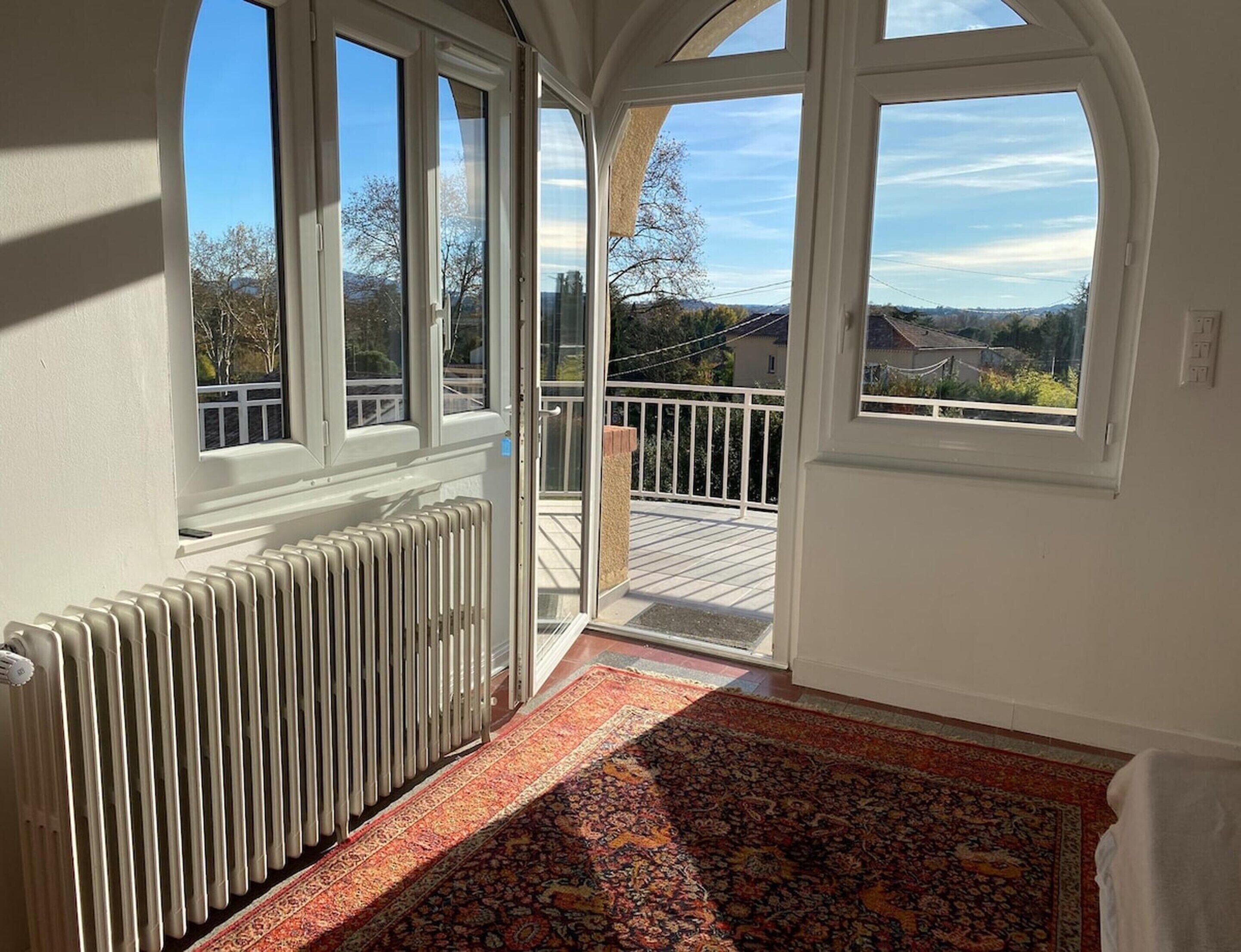 A room with a radiator, a patterned rug, and a view of a balcony with a railing.