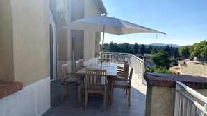 A balcony with a table and chairs, a large umbrella, and a view of the surrounding area. - Magnificent Family Villa Near the Ceze River (Saint-Ambroix)