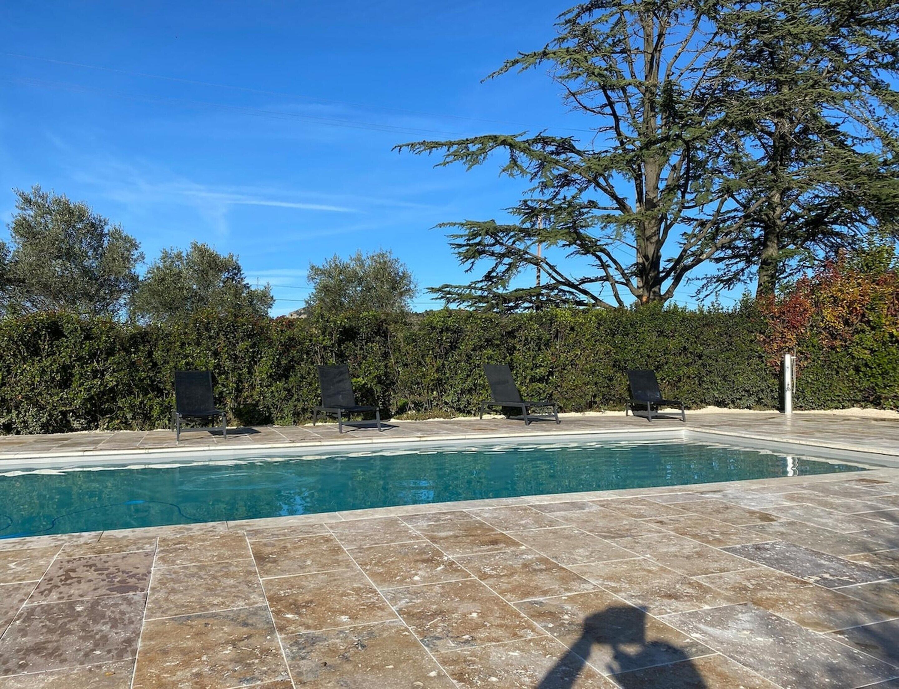 A swimming pool with tiled flooring, surrounded by trees and shrubs.