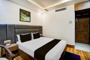 Een hotelkamer met een groot bed, hoofdeinde, nachtkastje met vaas en een houten deur.