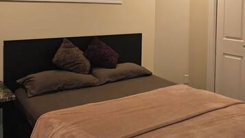 Une chambre à coucher avec un lit, une fenêtre avec des stores, une porte et un luminaire au plafond.