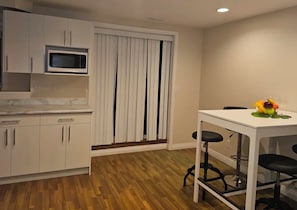 Una cocina con armarios blancos, microondas, suelo de madera y comedor con mesa y sillas.