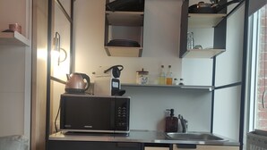 A compact kitchen with a microwave, kettle, and shelves above the counter. - Accommodation, terrace and secure, covered parking lot 5 minutes from Lille (Marcq-en-Barœul)