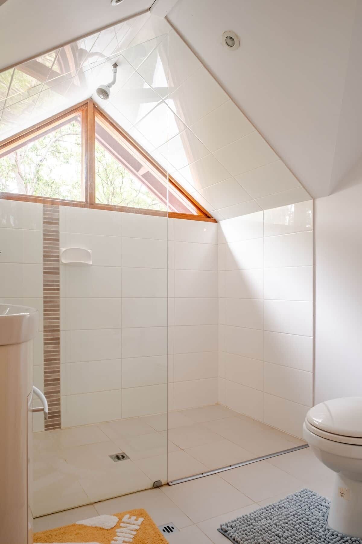 Une salle de bain moderne avec un puits de lumière, des carreaux blancs, une douche et des toilettes.