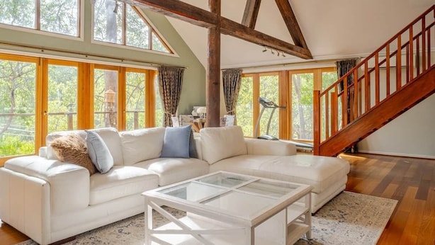 A spacious living room with a white sectional sofa, a glass coffee table, and a wooden staircase. - Bickley Tree Stay (Bickley)