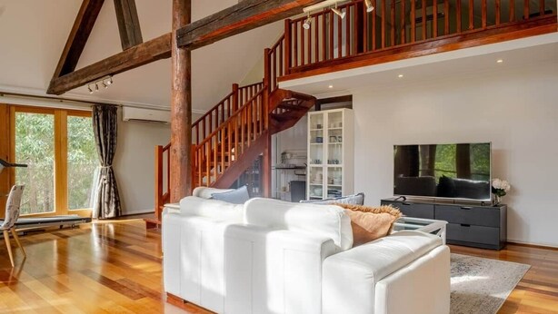 A spacious living room with a white sofa, wooden flooring, a staircase, and a television. - Bickley Tree Stay (Bickley)