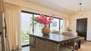 A modern kitchen with a central island, a dining area with a sofa, and large windows with curtains. - Private Hot Tub - 2BR in Nueva Escondida (San Miguel de Allende)