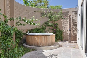 A wooden hot tub in a curved outdoor area with a brick wall, a door, and some greenery. - Private Hot Tub - 2BR in Nueva Escondida (San Miguel de Allende)