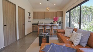 A modern living room with a sofa, a coffee table, and a kitchen area with wooden cabinets and a dining set. - Private Hot Tub - 2BR in Nueva Escondida (San Miguel de Allende)
