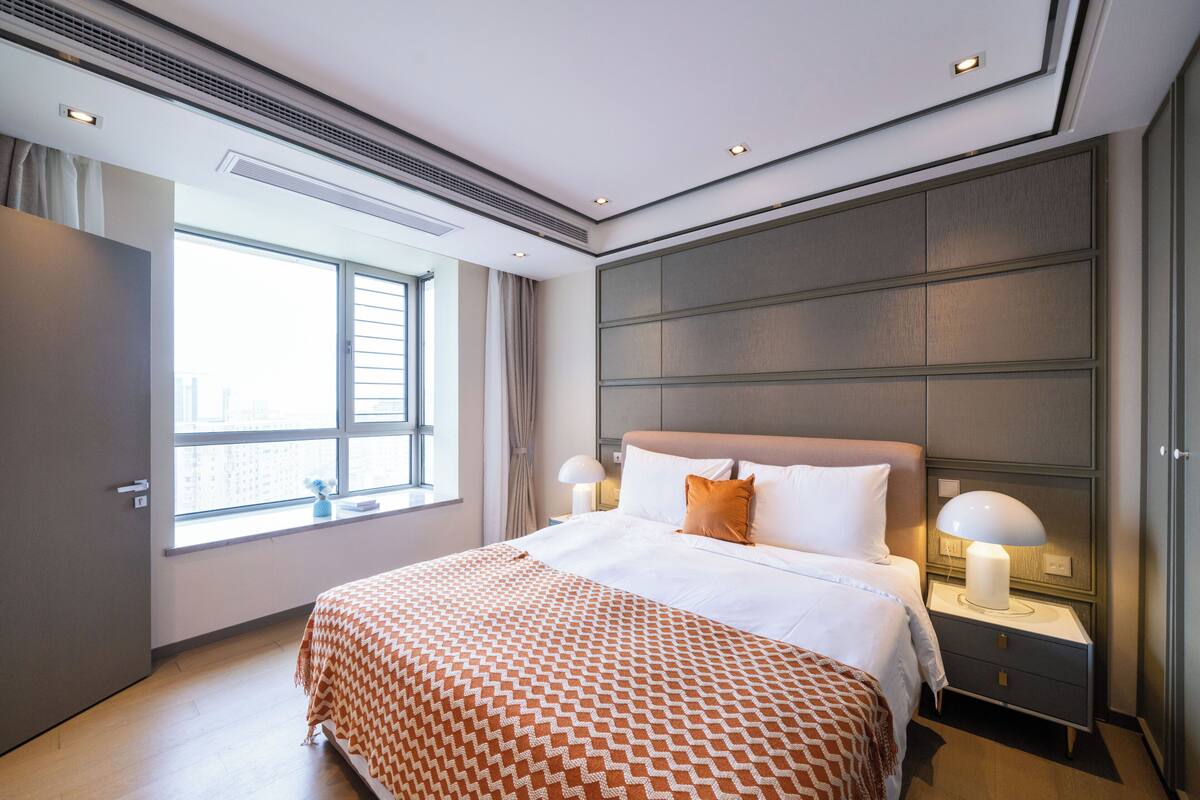 Habitación de hotel con una cama grande, lámparas de noche, un ventanal y vistas a la ciudad.