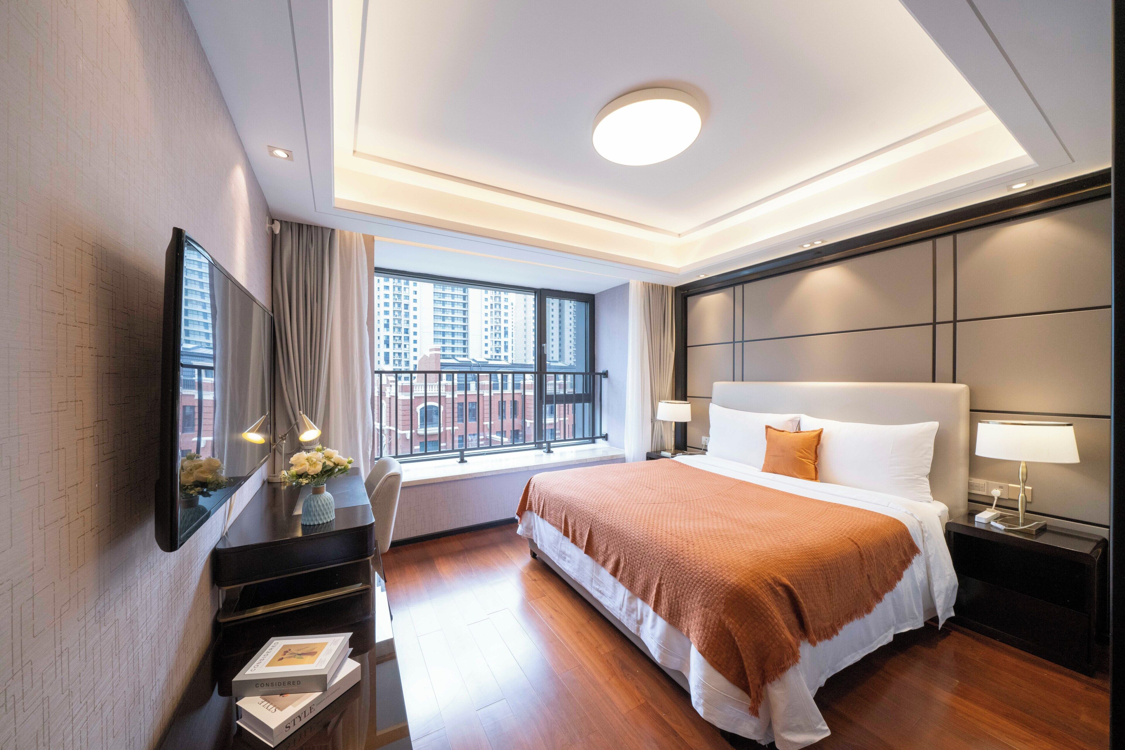 A hotel room with a large bed, a desk, a flat-screen TV, and a window with a city view.