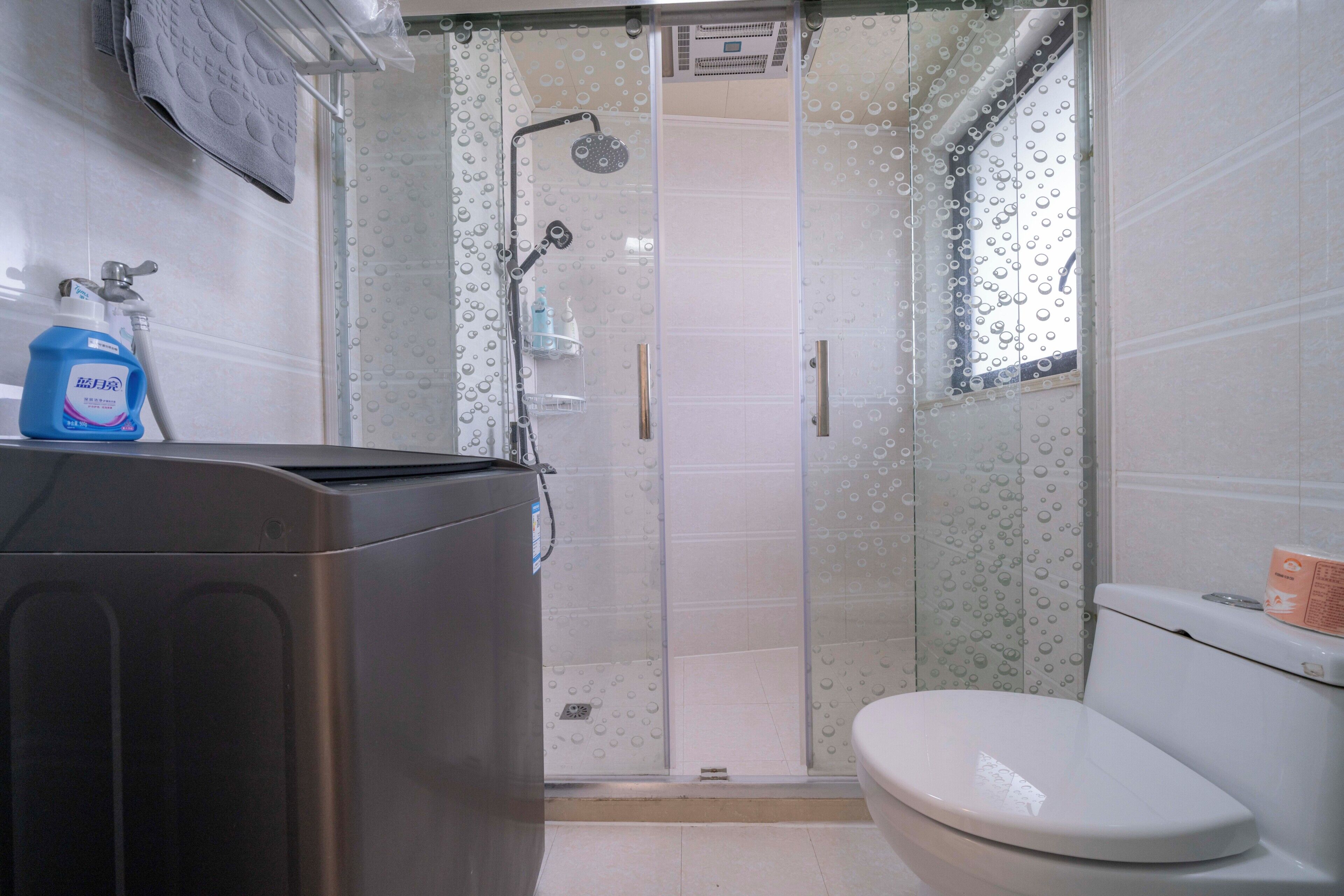A bathroom with a shower, toilet, and a washing machine.