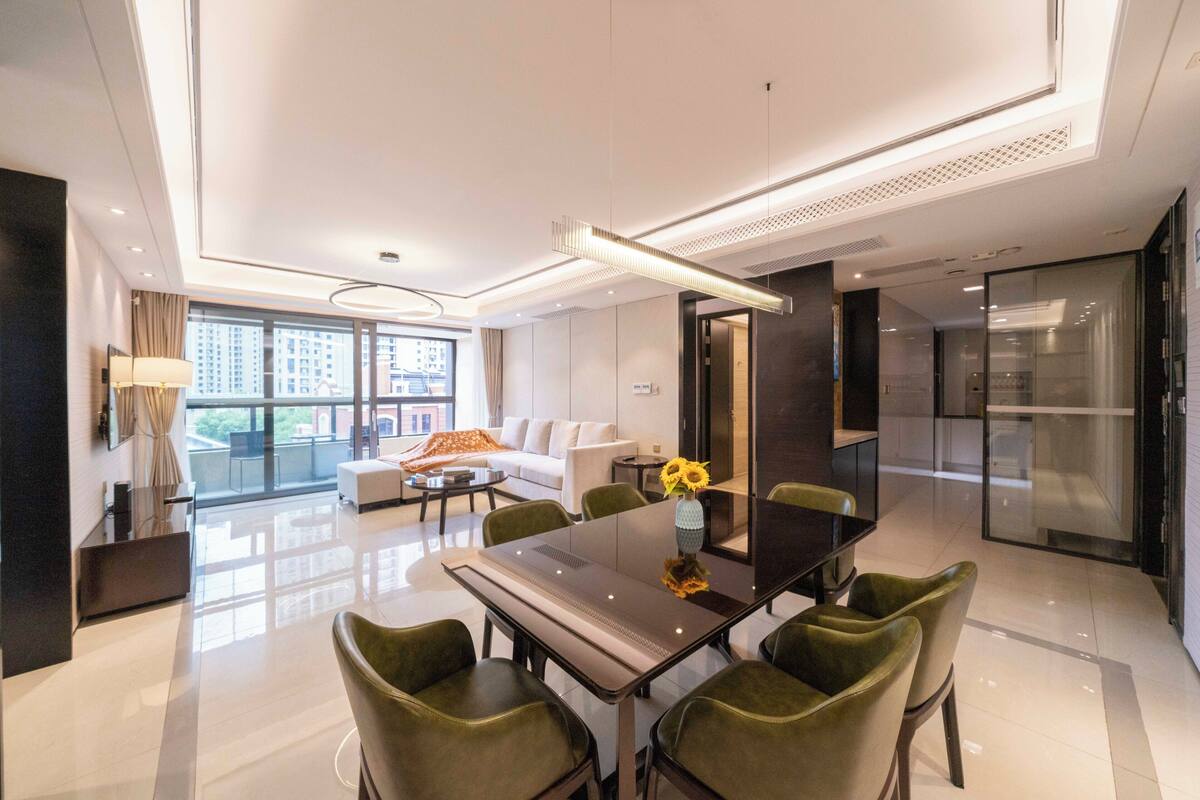 Una habitación de hotel moderna con zona de comedor, sofá, mesa de centro y un amplio ventanal con vista a la ciudad.