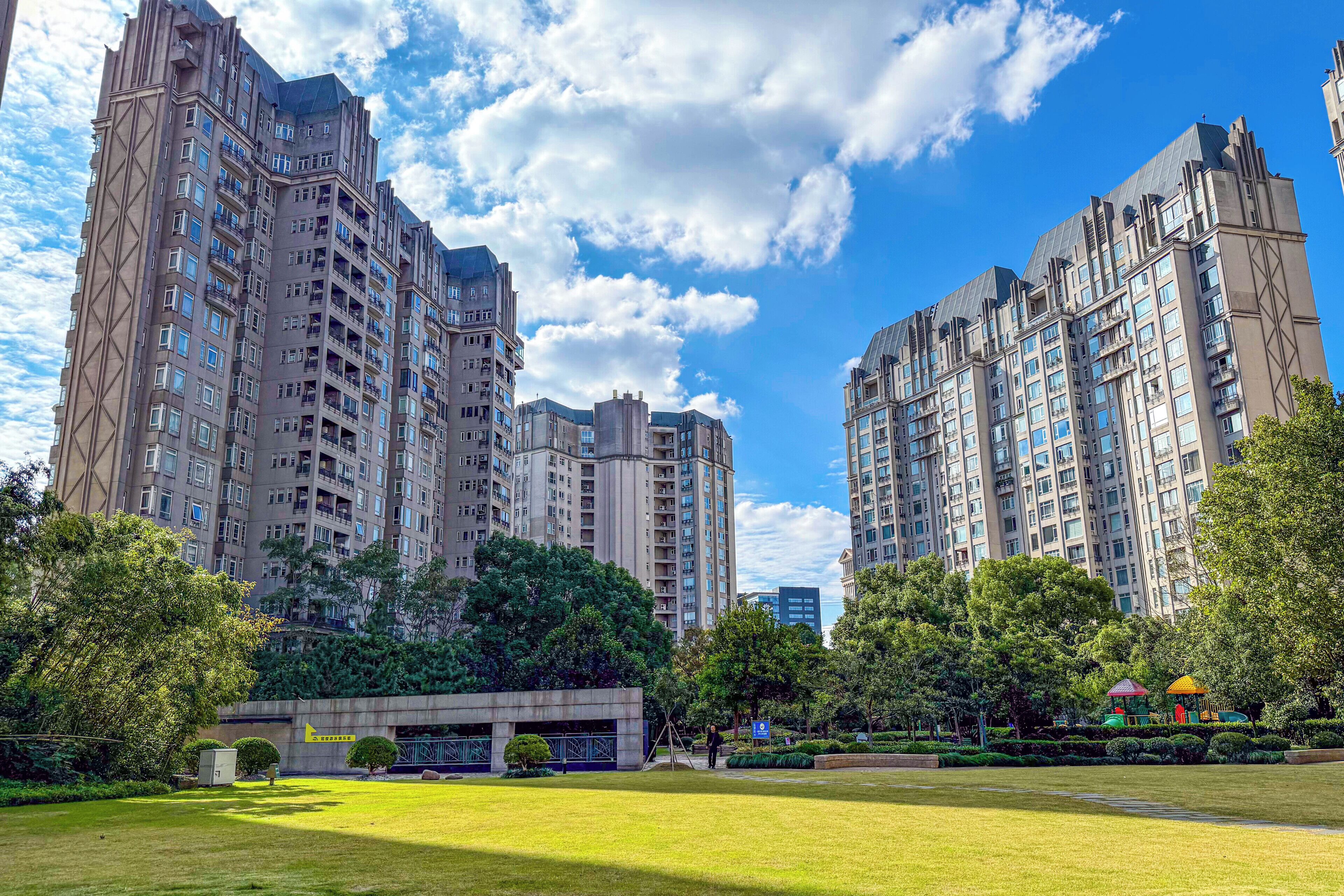 A high-rise residential building complex with multiple floors, a well-maintained lawn, and a playground area.